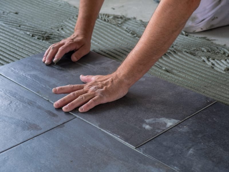 Worker's hands pressing ceramic floor tiles laid on applied adhesive